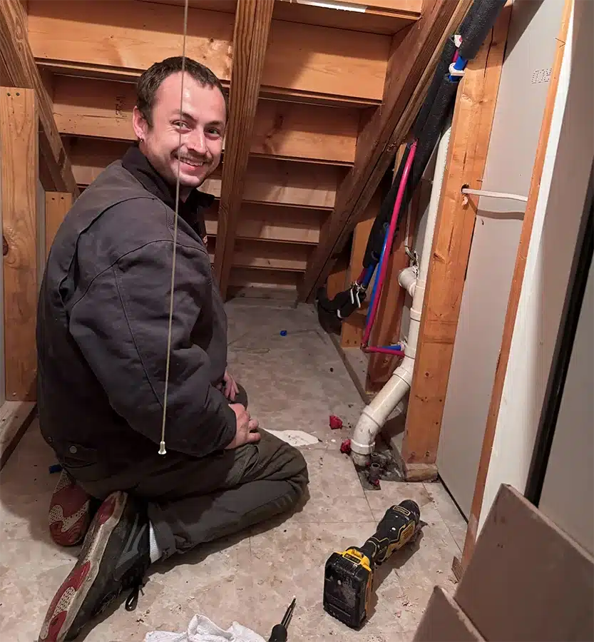 Kinsmen plumber working on pipes under a staircase in a Summerville area home